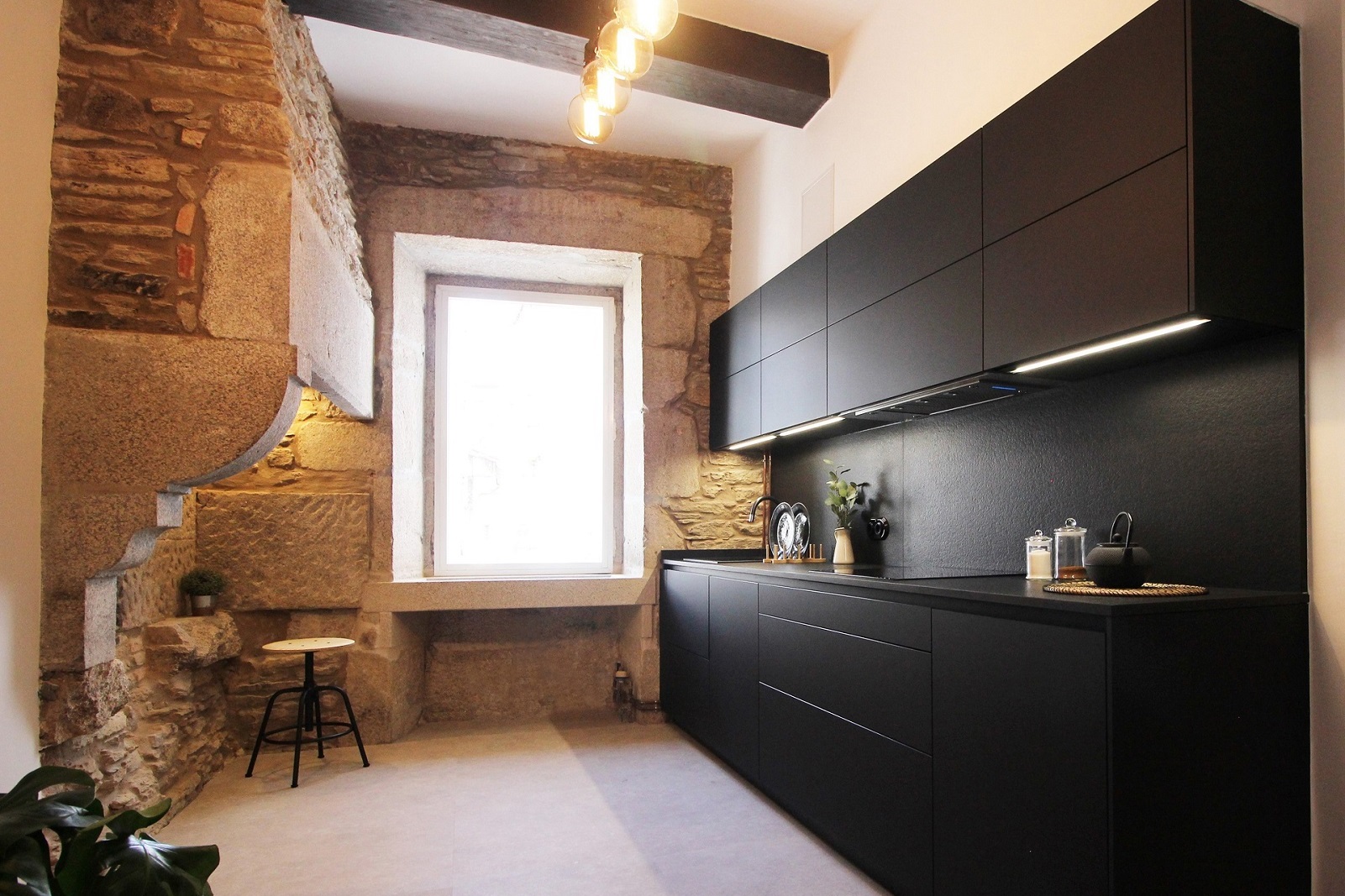 Cocina de Santiago Interiores con pared de piedra y muebles en negro